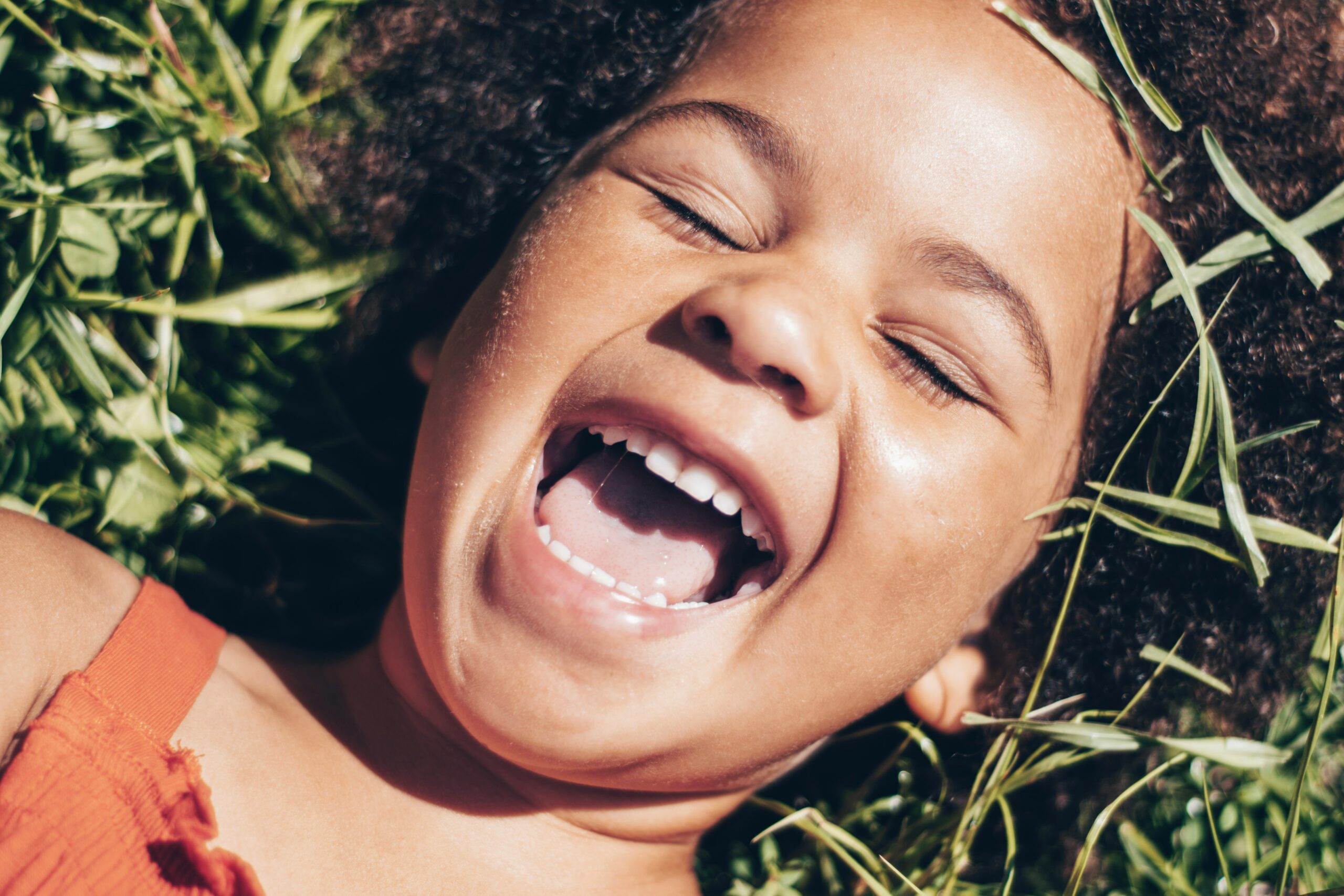 Happy girl laughing in grass for fun and physical outdoor family adventure