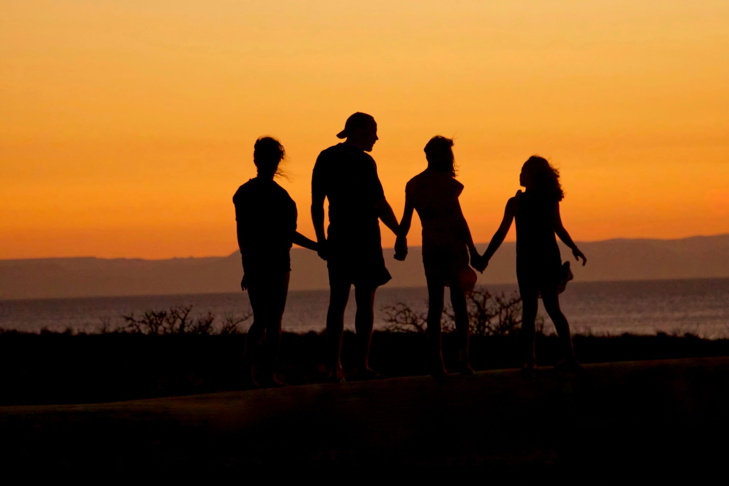 family with teenagers holding hands in sunset